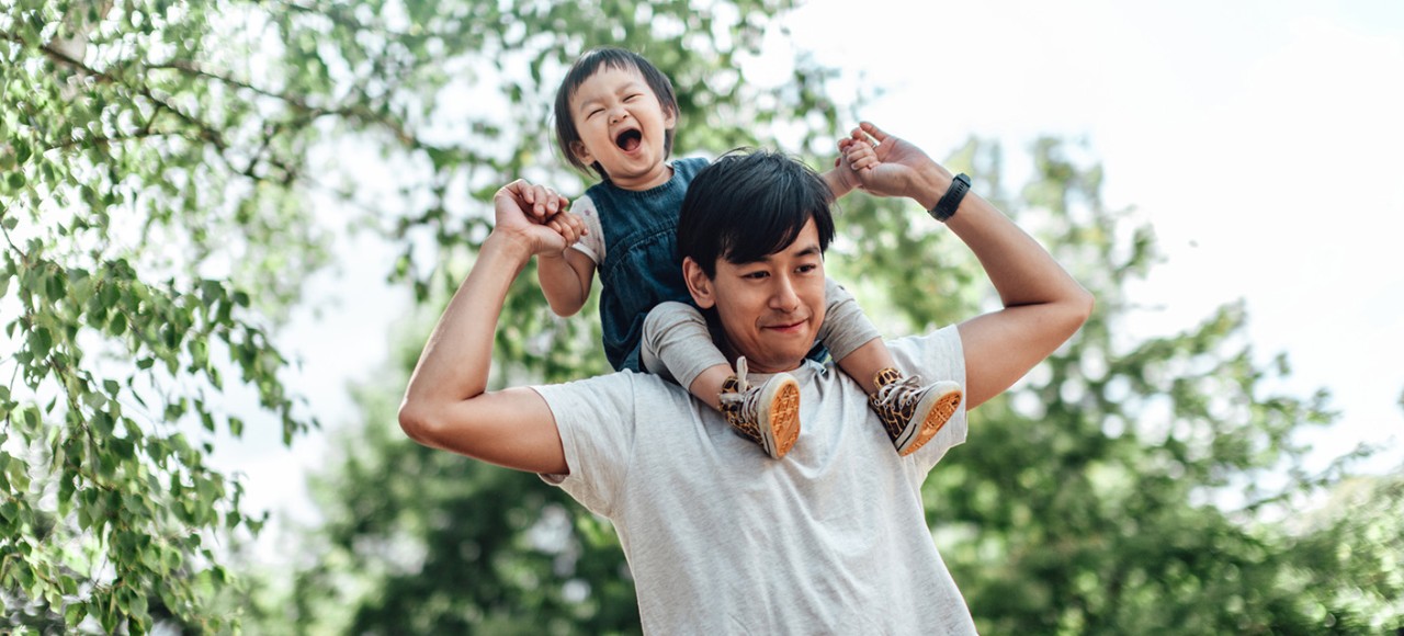 Low angel view of an Asian dad carrying daughter on his shoulder. Father daughter bonding time. Family love, care concepts.